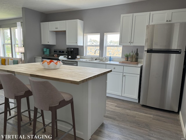 kitchen with light hardwood / wood-style flooring, a kitchen island, white cabinets, stainless steel refrigerator, and sink