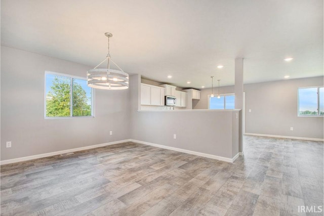 spare room featuring light wood-type flooring, plenty of natural light, and an inviting chandelier