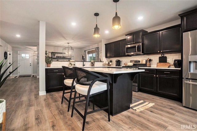 kitchen with a breakfast bar, appliances with stainless steel finishes, light hardwood / wood-style floors, decorative light fixtures, and kitchen peninsula