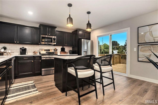 kitchen with backsplash, stainless steel appliances, light hardwood / wood-style flooring, and decorative light fixtures