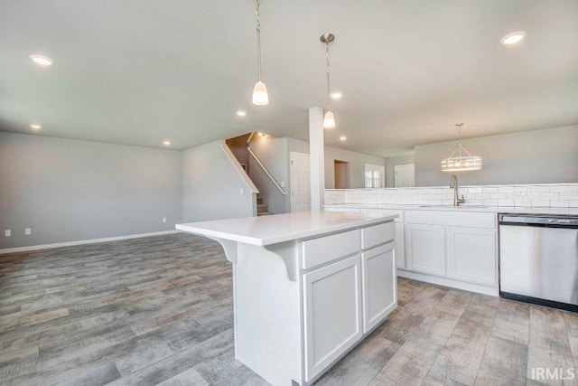 kitchen with a center island, decorative light fixtures, light wood-type flooring, stainless steel dishwasher, and tasteful backsplash