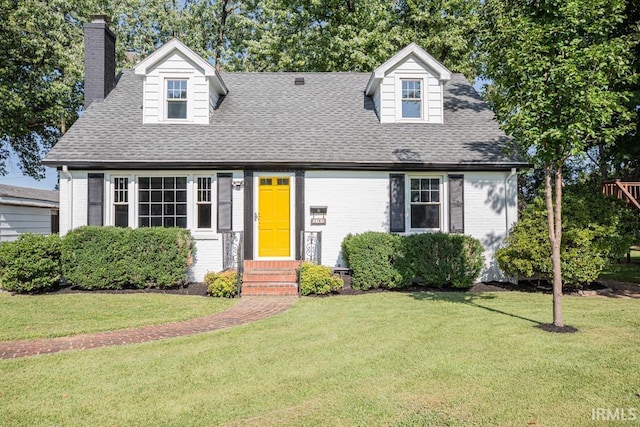 new england style home featuring brick siding, a chimney, a front lawn, and roof with shingles