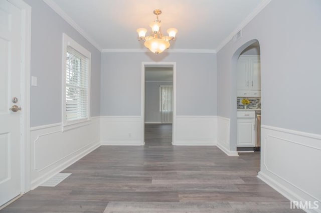 unfurnished dining area featuring crown molding, a wainscoted wall, dark wood finished floors, and an inviting chandelier