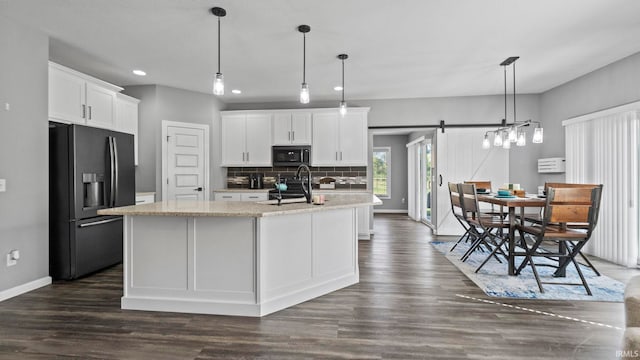 kitchen with a barn door, decorative backsplash, stainless steel appliances, white cabinetry, and a sink