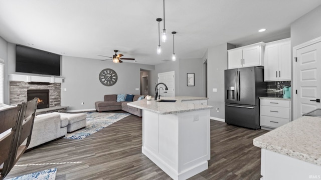 kitchen with a stone fireplace, a sink, white cabinetry, black refrigerator with ice dispenser, and an island with sink