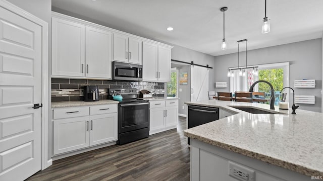 kitchen with a barn door, a sink, white cabinetry, backsplash, and black appliances