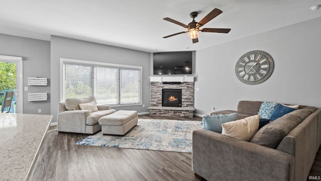 living room featuring a stone fireplace, dark wood-style flooring, and a wealth of natural light