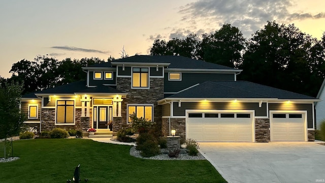 prairie-style house featuring an attached garage, stone siding, a front lawn, and concrete driveway