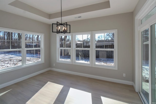 unfurnished dining area with a notable chandelier, a tray ceiling, light hardwood / wood-style flooring, and a wealth of natural light