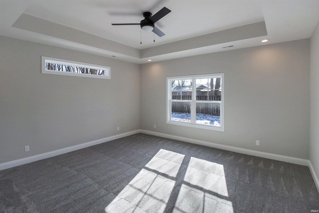 spare room featuring ceiling fan, a raised ceiling, and dark carpet