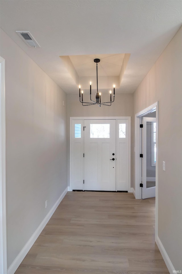 entryway featuring a tray ceiling, light hardwood / wood-style flooring, and a chandelier