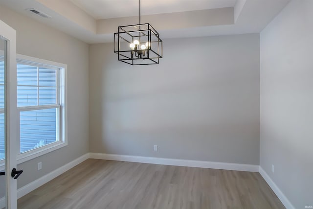 unfurnished dining area with light hardwood / wood-style floors, a raised ceiling, and a chandelier