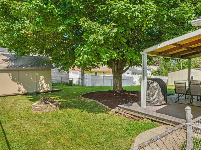 view of yard with fence, a wooden deck, an outdoor fire pit, an outdoor structure, and a storage unit