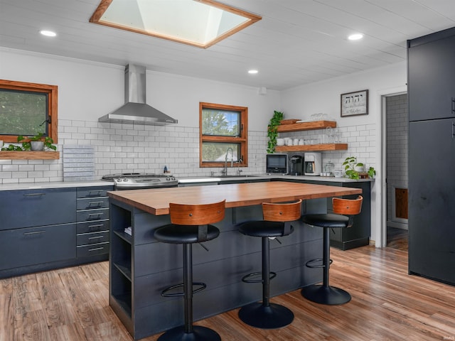 kitchen with open shelves, wooden counters, a sink, and wall chimney range hood