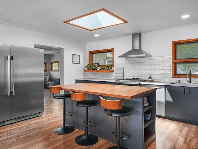 kitchen with a sink, open shelves, stainless steel appliances, wall chimney exhaust hood, and butcher block counters