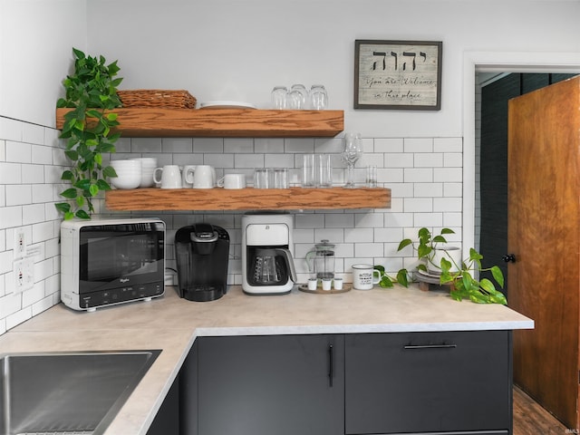 kitchen featuring open shelves, backsplash, a sink, and light countertops