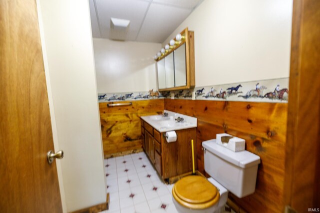 bathroom featuring wood walls, toilet, vanity, and tile patterned floors