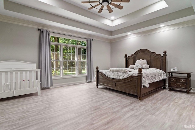 bedroom featuring ceiling fan, crown molding, a tray ceiling, and light hardwood / wood-style floors