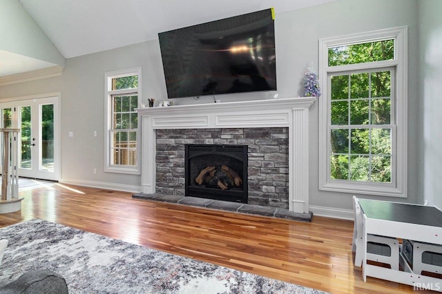 living room with vaulted ceiling, hardwood / wood-style flooring, a stone fireplace, and french doors