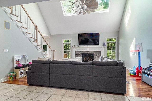 living room featuring high vaulted ceiling, a fireplace, a skylight, light hardwood / wood-style flooring, and ceiling fan