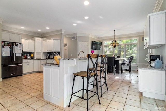 kitchen featuring black fridge, white cabinets, a center island, and light tile patterned flooring