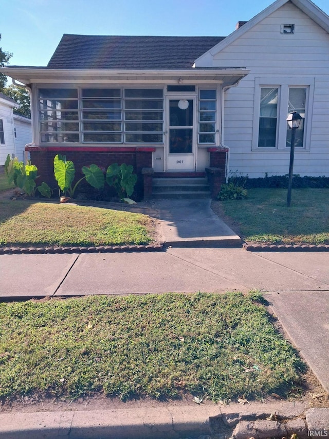 view of front of house with entry steps, a sunroom, a shingled roof, and a front lawn