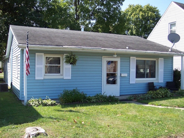 view of front of home featuring a shingled roof, a front yard, and central AC