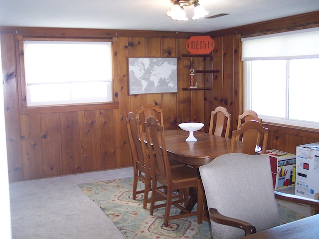 dining area featuring carpet flooring, plenty of natural light, and wood walls