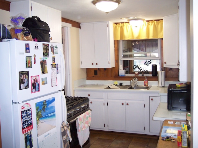 kitchen with white cabinets, freestanding refrigerator, gas range oven, light countertops, and a sink