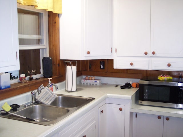 kitchen with light countertops, white cabinets, stainless steel microwave, and a sink