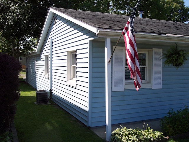 view of side of home with central AC, a yard, and a shingled roof