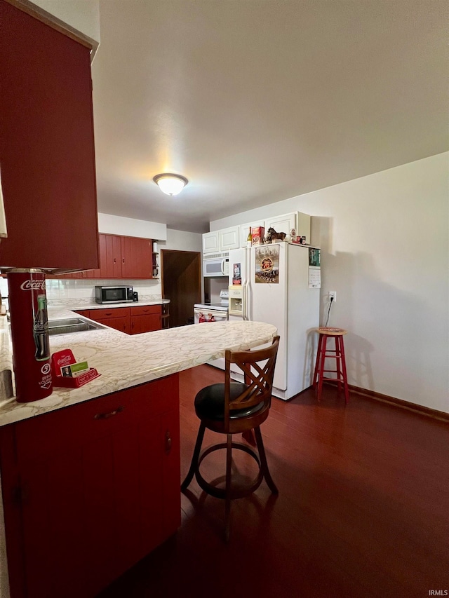 kitchen featuring a breakfast bar, kitchen peninsula, dark wood-type flooring, and white appliances