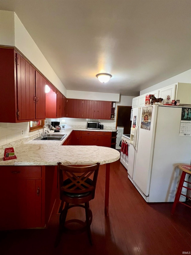 kitchen featuring dark wood-type flooring, a breakfast bar, sink, kitchen peninsula, and white appliances