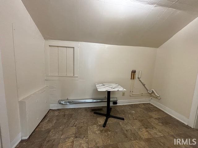 interior space featuring lofted ceiling, stone finish flooring, and baseboards