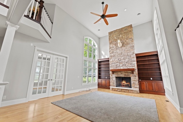 unfurnished living room featuring french doors, ceiling fan, high vaulted ceiling, wood finished floors, and a fireplace