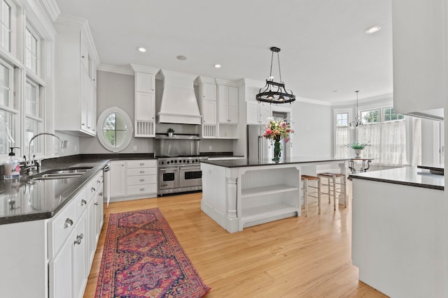 kitchen featuring light wood finished floors, a sink, custom range hood, open shelves, and stainless steel appliances