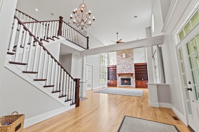 foyer featuring wood finished floors, ceiling fan with notable chandelier, stairway, baseboards, and a stone fireplace