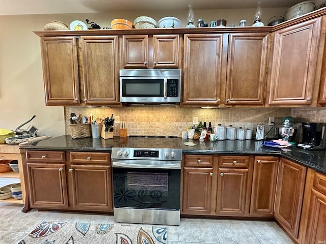 kitchen featuring backsplash, stainless steel appliances, light tile patterned floors, and dark stone counters