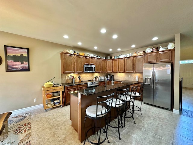 kitchen featuring appliances with stainless steel finishes, backsplash, dark stone counters, a breakfast bar area, and light tile patterned flooring