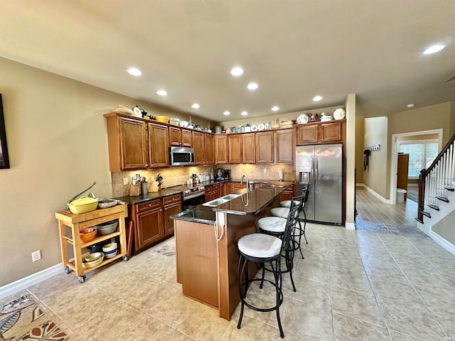 kitchen featuring dark stone counters, tasteful backsplash, a kitchen bar, appliances with stainless steel finishes, and sink