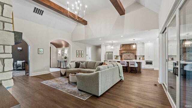 living room with arched walkways, dark wood finished floors, beam ceiling, and an inviting chandelier