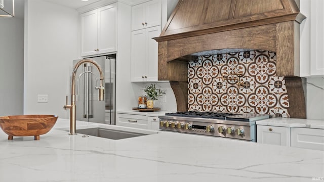 kitchen featuring premium range hood, stove, white cabinets, light stone countertops, and tasteful backsplash