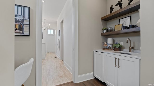 interior space with sink, an inviting chandelier, hardwood / wood-style flooring, and white cabinetry