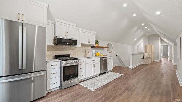 kitchen with hardwood / wood-style floors, sink, appliances with stainless steel finishes, decorative backsplash, and lofted ceiling