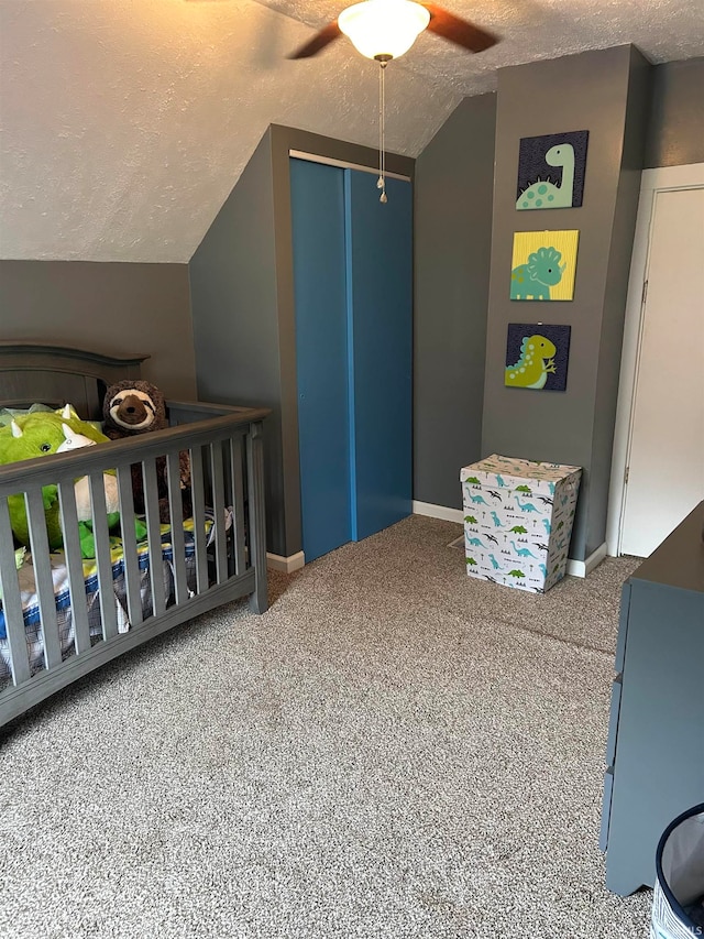 carpeted bedroom with lofted ceiling, ceiling fan, a crib, and a textured ceiling