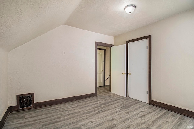 additional living space featuring lofted ceiling, hardwood / wood-style floors, and a textured ceiling