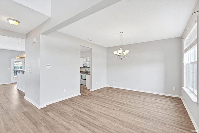 spare room featuring plenty of natural light, a chandelier, and light hardwood / wood-style flooring