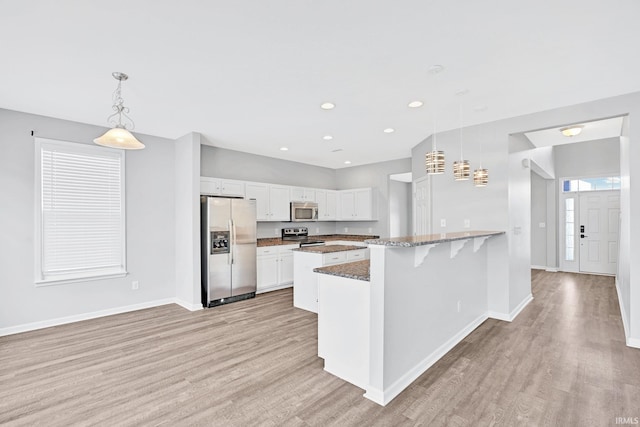 kitchen with white cabinetry, hanging light fixtures, stainless steel appliances, and a breakfast bar