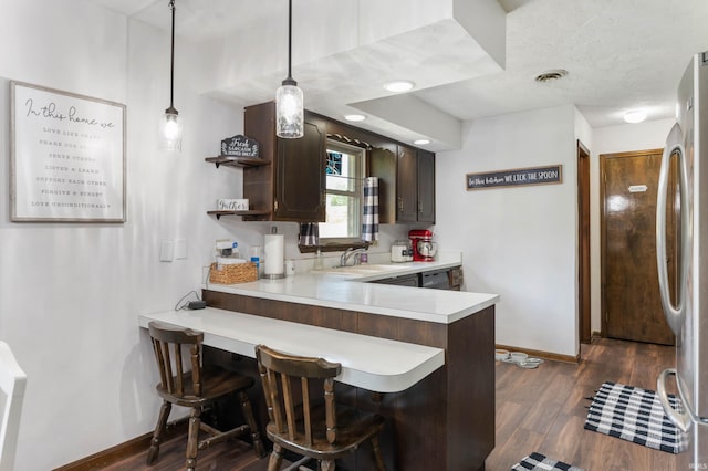 kitchen with sink, stainless steel fridge, wood-type flooring, dark brown cabinetry, and a breakfast bar