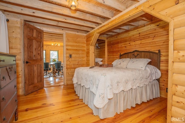 bedroom featuring beam ceiling, wood walls, and light wood-style flooring